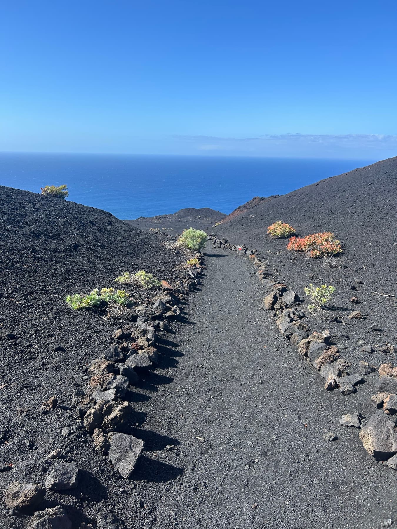 Black volcanic trail descending toward the sea
